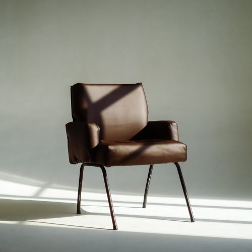 Stylish leather armchair in sunlight over white wall background.